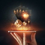 Creative background, online casino, in a man’s hand a smartphone with playing cards, roulette and chips, black-gold background. Internet gambling concept. Copy space