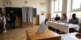 Volební místnost ve škole s urnou, plentou a volební komisí