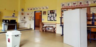 Volební místnost ve třídě základní školy s bílou volební urnou a plentou