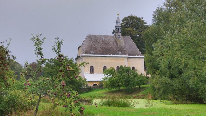 Venkovský kostel na kopci mezi stromy a zahradou Venkovský kostel na kopci mezi stromy a zahradou